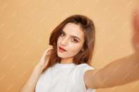 brunette-girl-with-long-hair-dressed-white-t-shirt-makes-selfie-beige-background-studio472597-1336.jpg