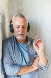 senior-man-leaning-wall-listening-music-headphone23-2147859692.jpg