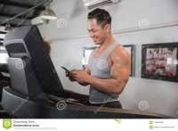 asian-muscular-man-treadmill-gym-centre-holding-smartphone-[...].jpg